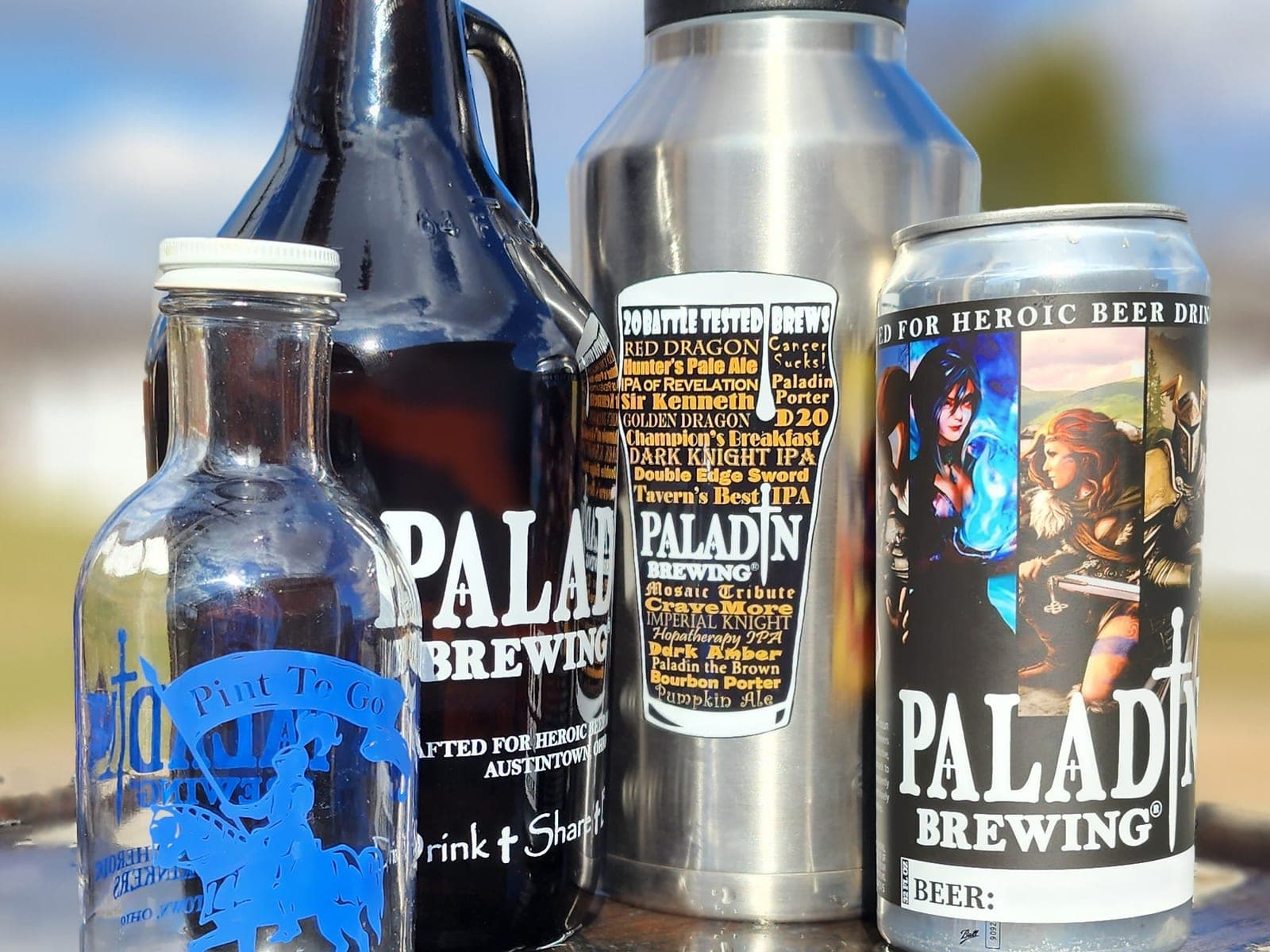 A Paladin Brewing Pint To Go bottle, glass growler, steel growler and crowler can lined up outside in the sun
